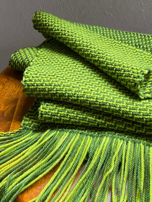 Green color-and-weave twill scarf draped on a stool.