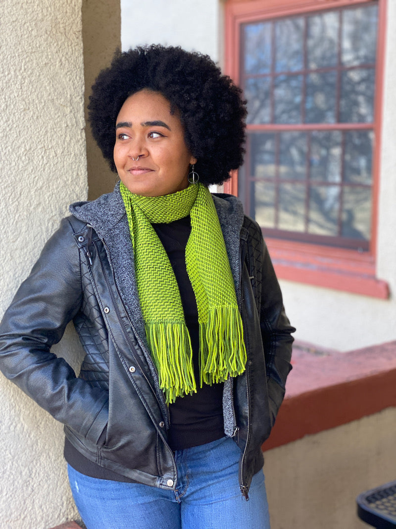 Dana wearing the green color-and-weave scarf outside leaning against a building. 