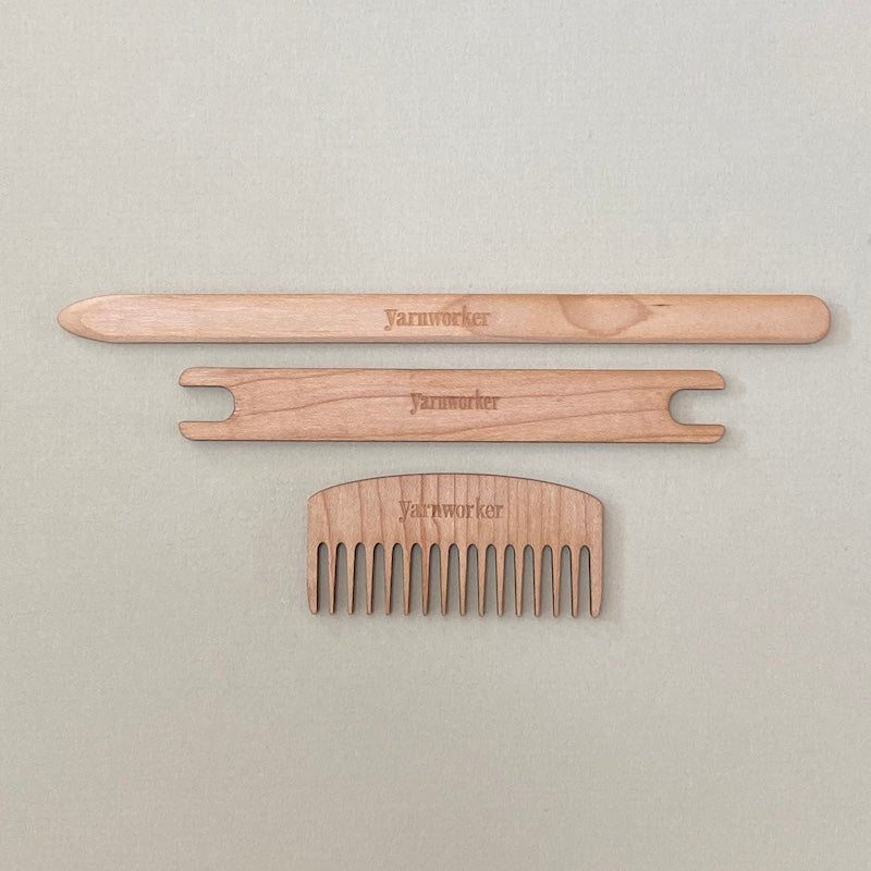 A pick-up stick, shuttle, and mini comb laying flat on a table.