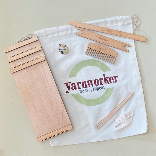 Size 8, 10, 12 mini looms with comb, pick-up stick, mini shuttle, weaving needle, and enamel pin all resting on a cloth Yarnworker project bag.
